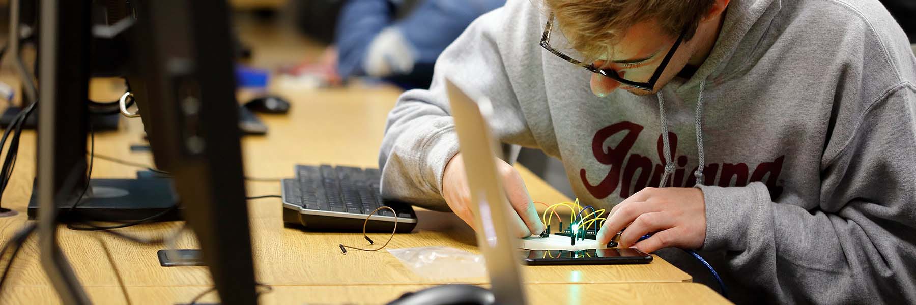 A student works on computer hardware, with circuits and wires, in a computer lab.